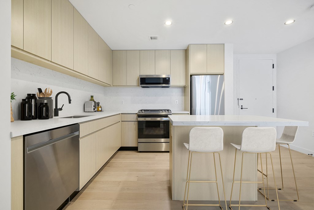 a kitchen with white cabinets and a island with three stools at The Paxton, Brooklyn, NY 11201